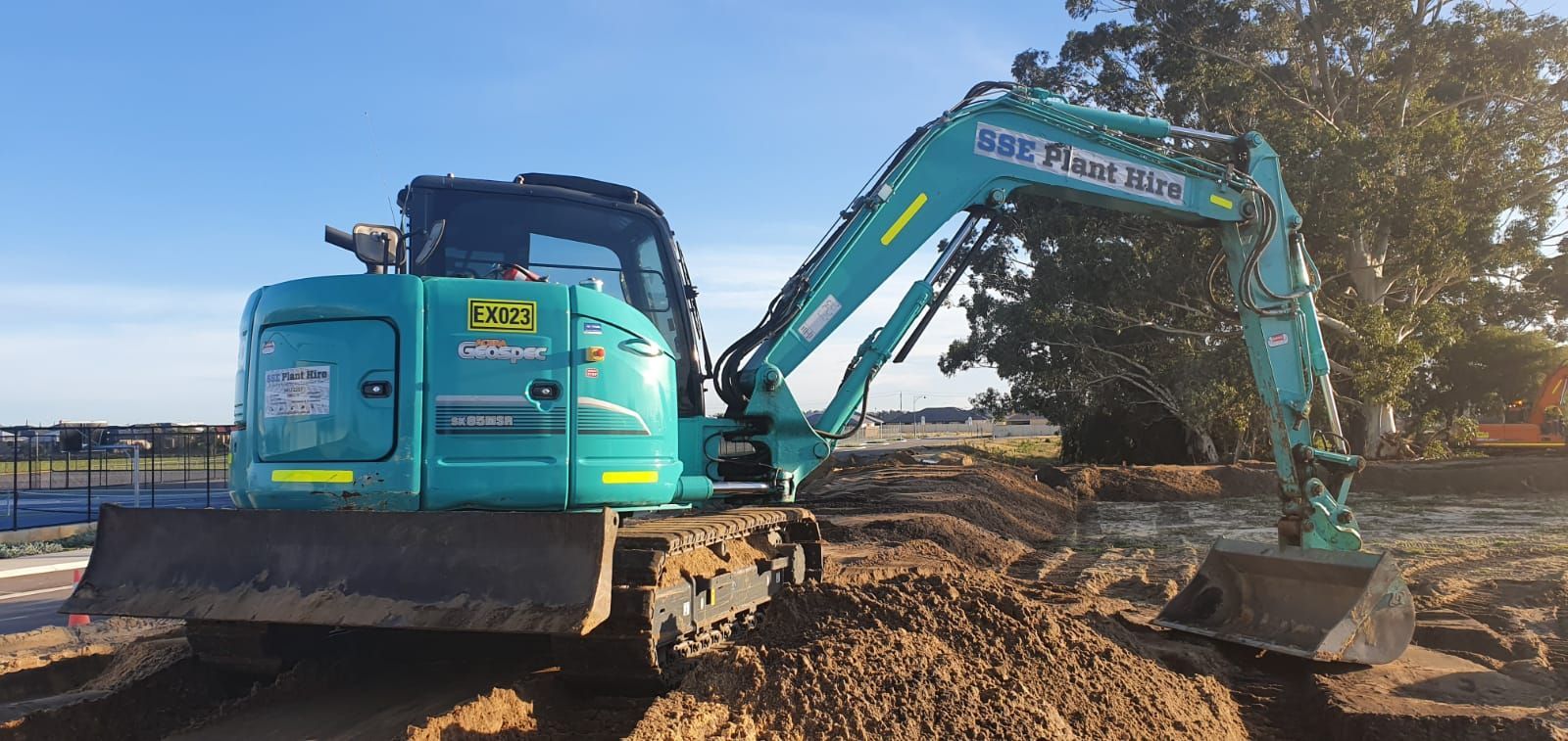 A blue and green excavator is sitting on top of a pile of dirt.