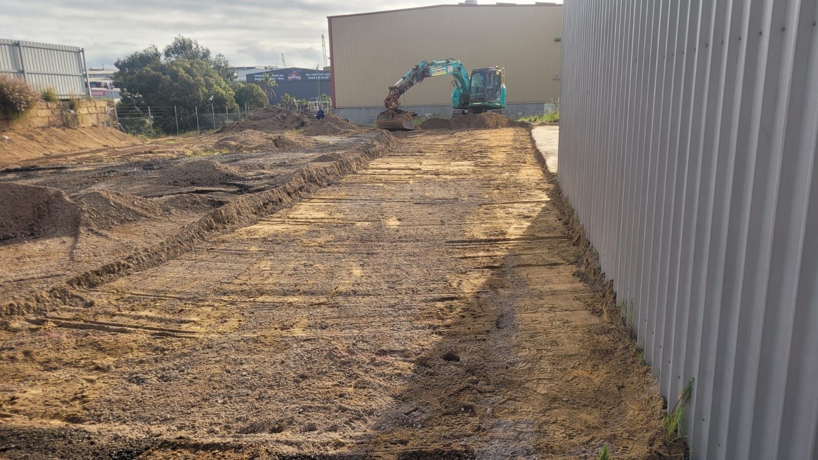 A large excavator is digging in a dirt field next to a building.