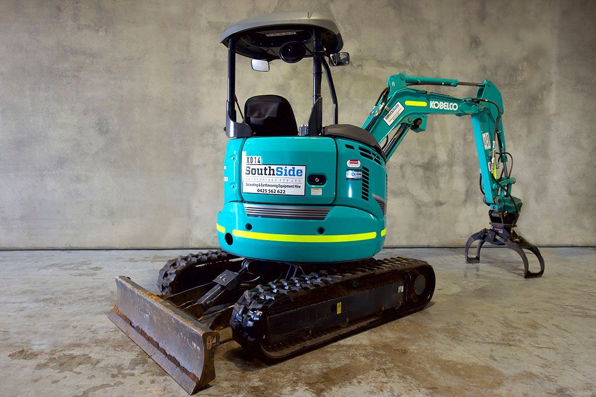 A small blue and yellow excavator is sitting on a concrete floor.