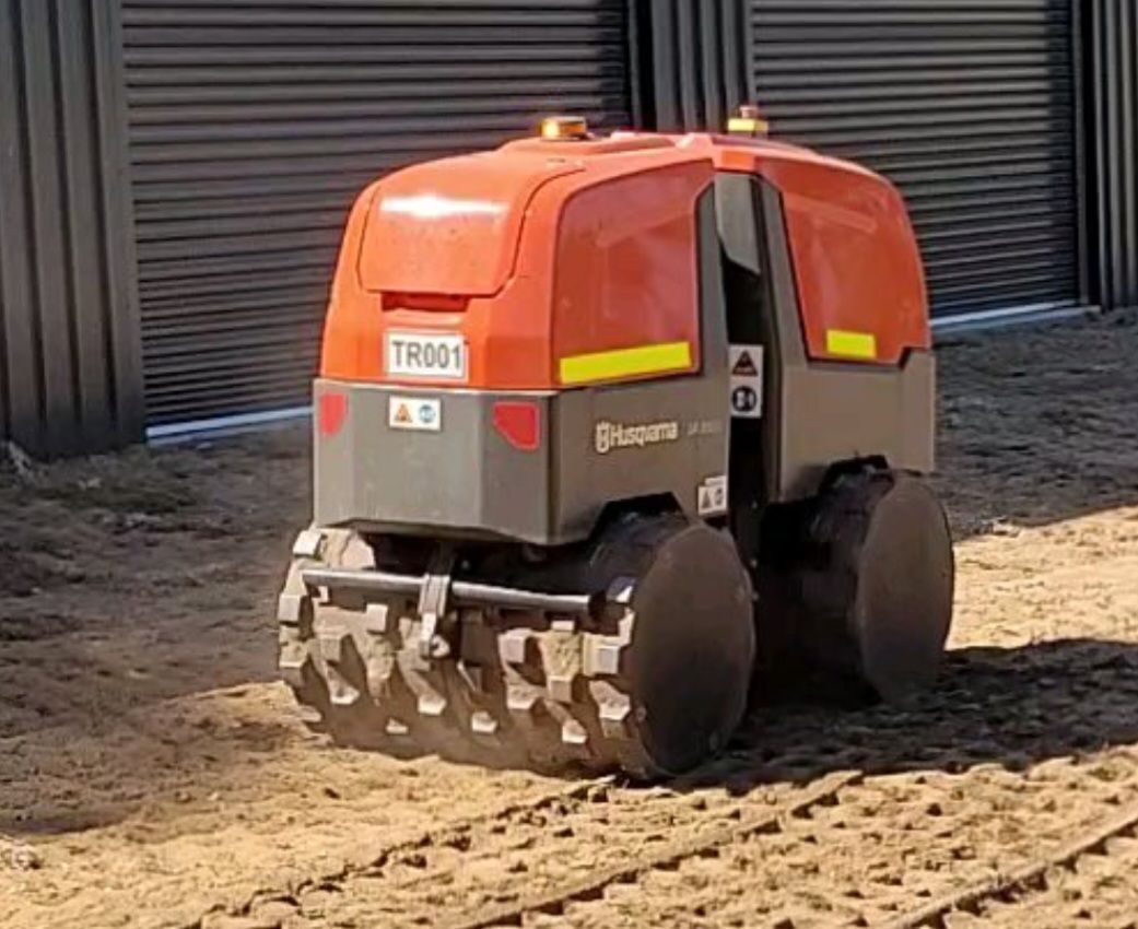 A small orange and black machine is sitting on top of a dirt field.