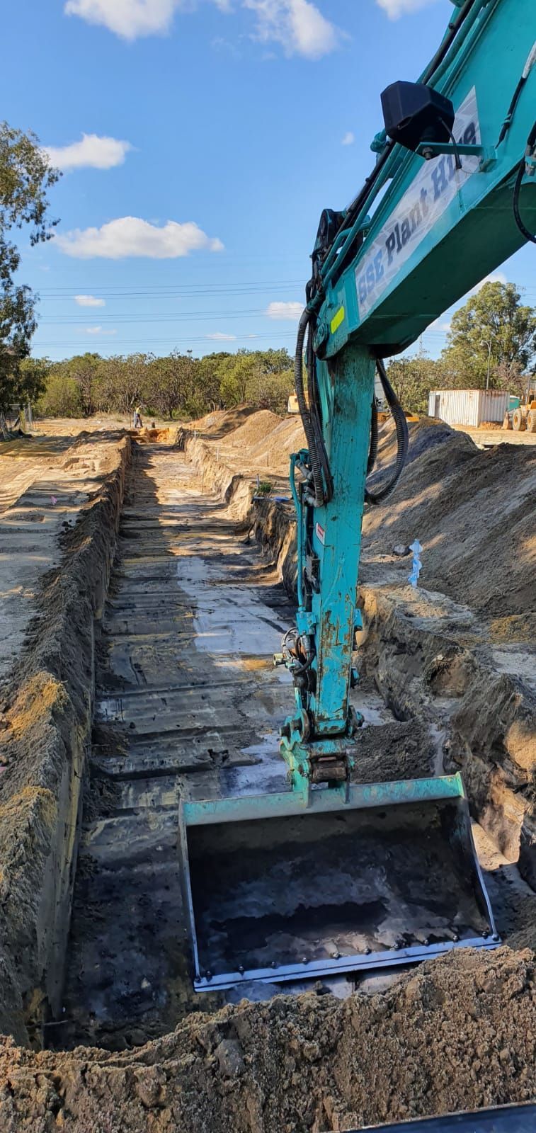 A green excavator is digging a hole in the ground.