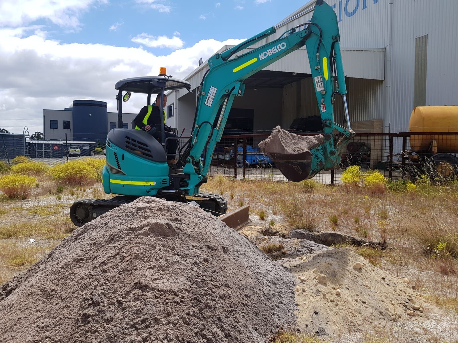 A small excavator is sitting on top of a pile of dirt in a field.