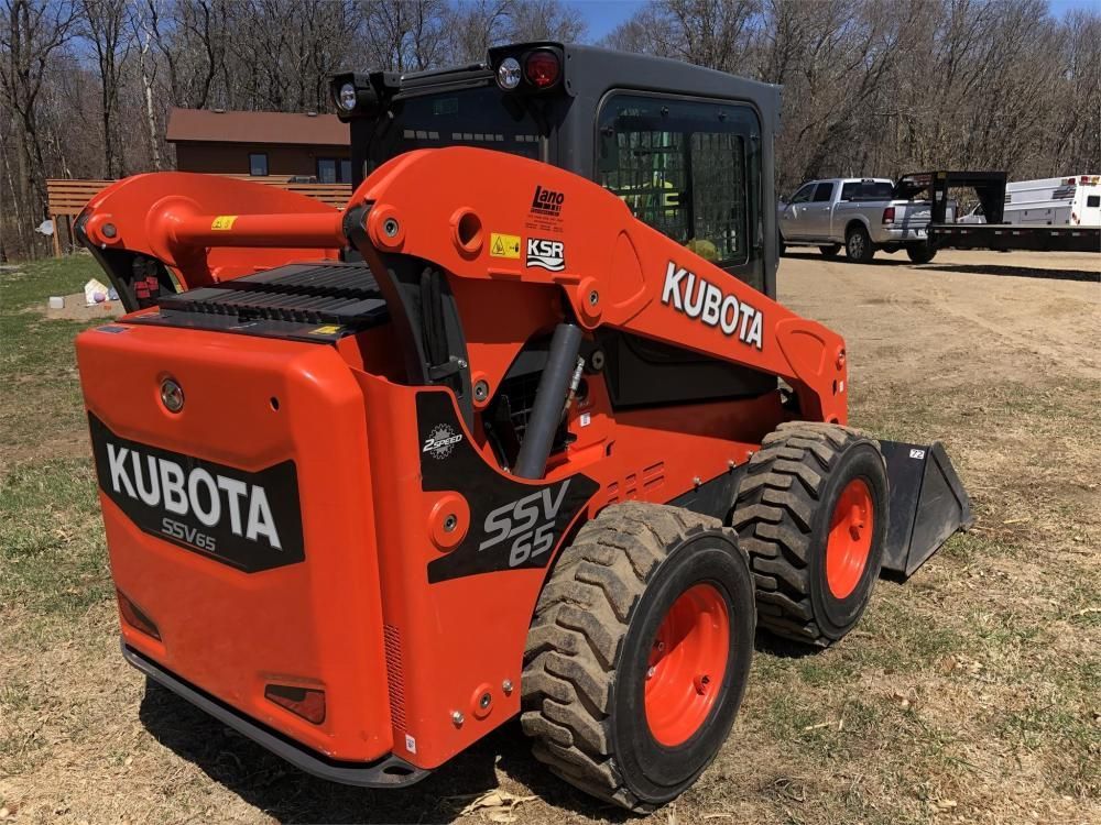 A red and black kubota skid steer is parked in a dirt field.