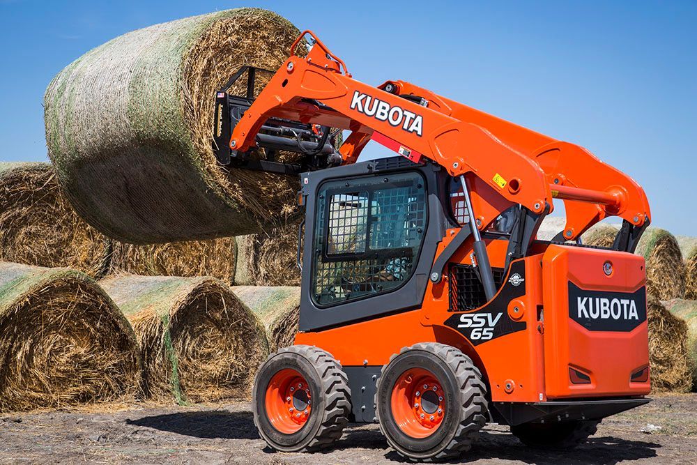 A kubota skid steer is lifting a bale of hay.