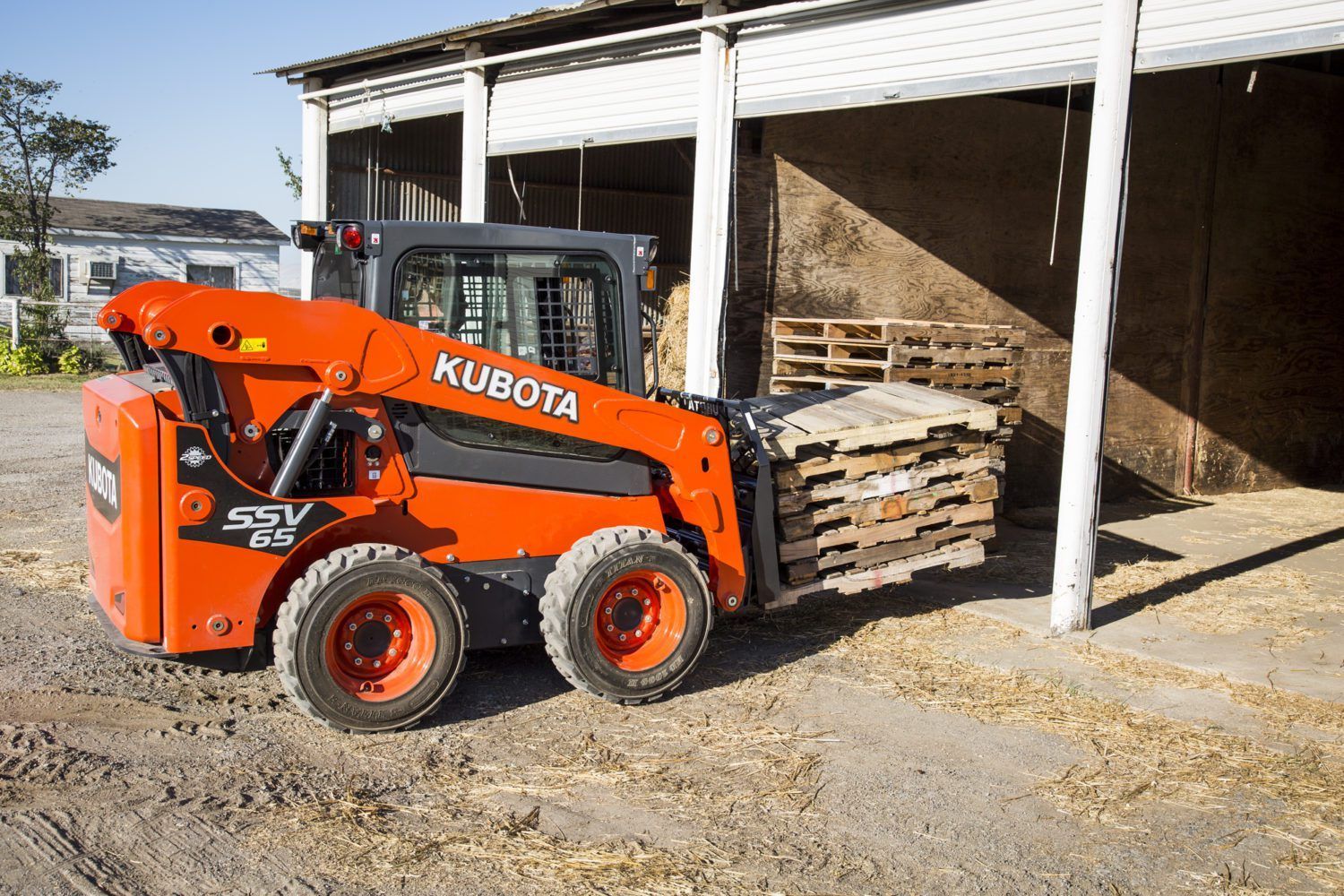 A kubota skid steer is parked in front of a barn.