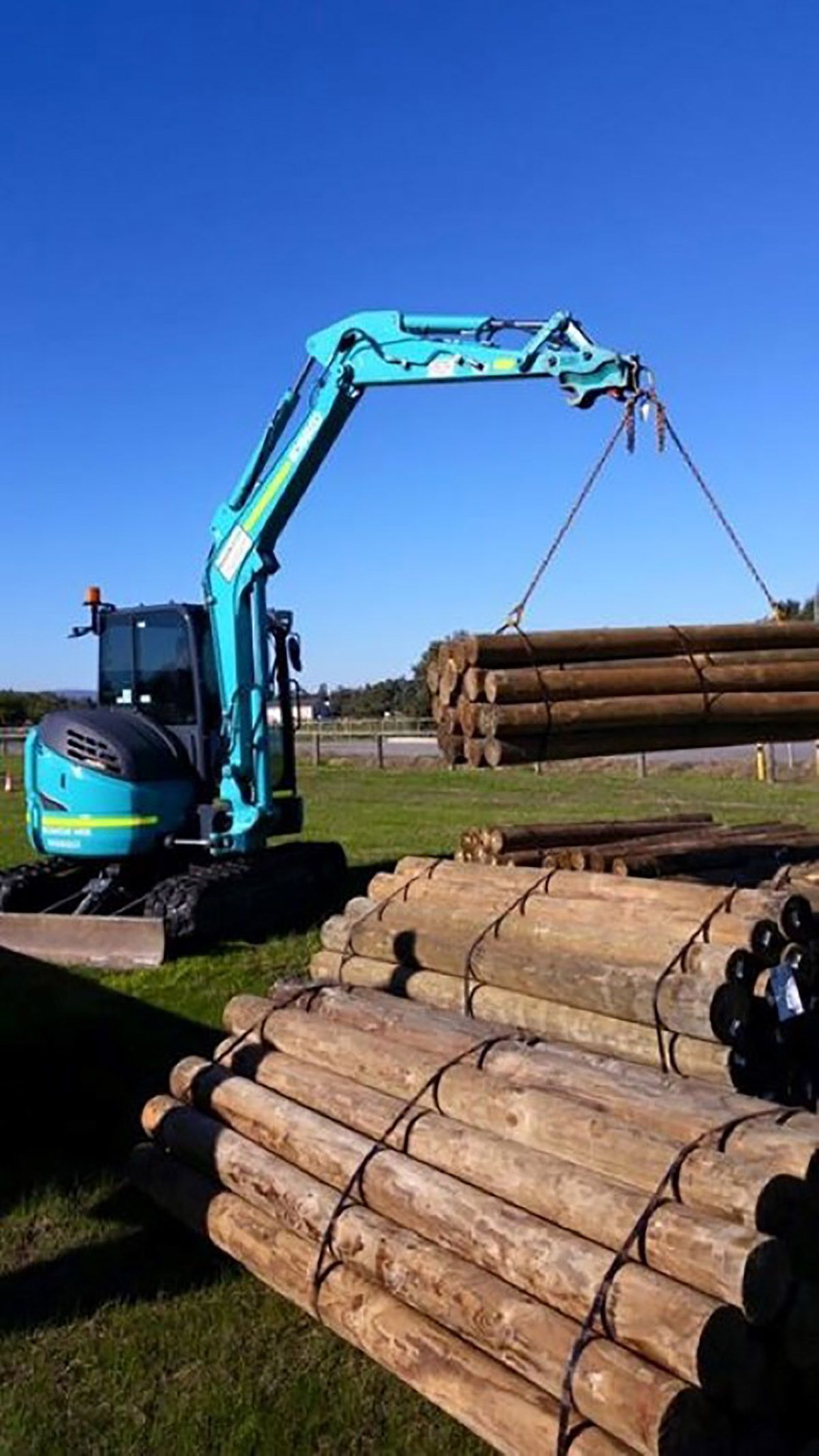 A crane is lifting a pile of logs in a field.