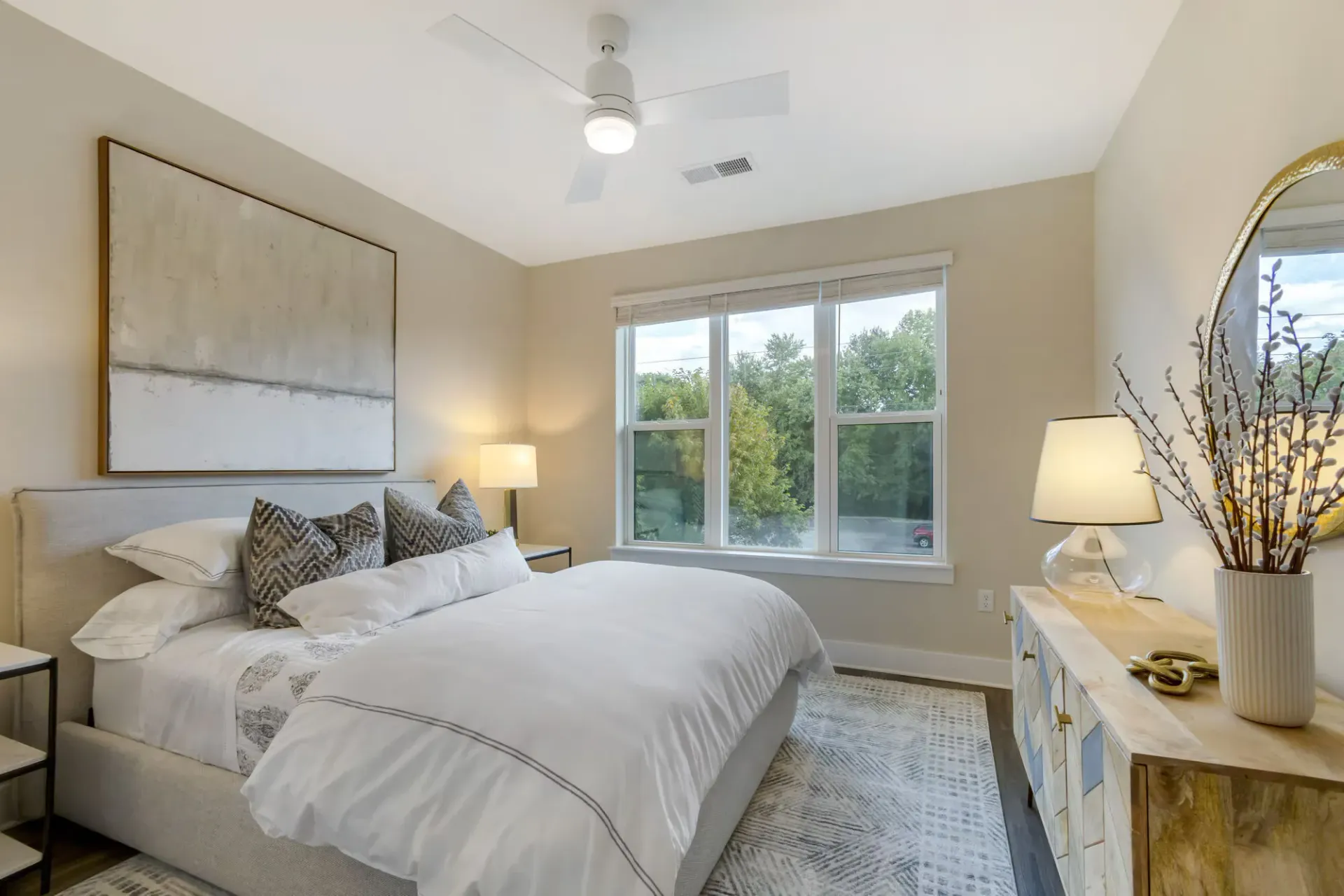 Bright bedroom with a king bed, neutral decor, two nightstands, dresser, and large window.