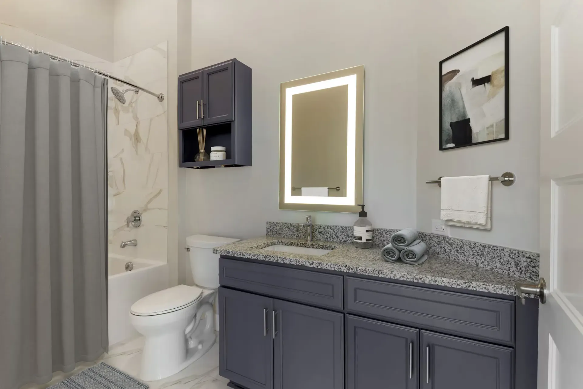 Bathroom with navy-blue vanity, granite countertop, backlit mirror, and a gray shower curtain.