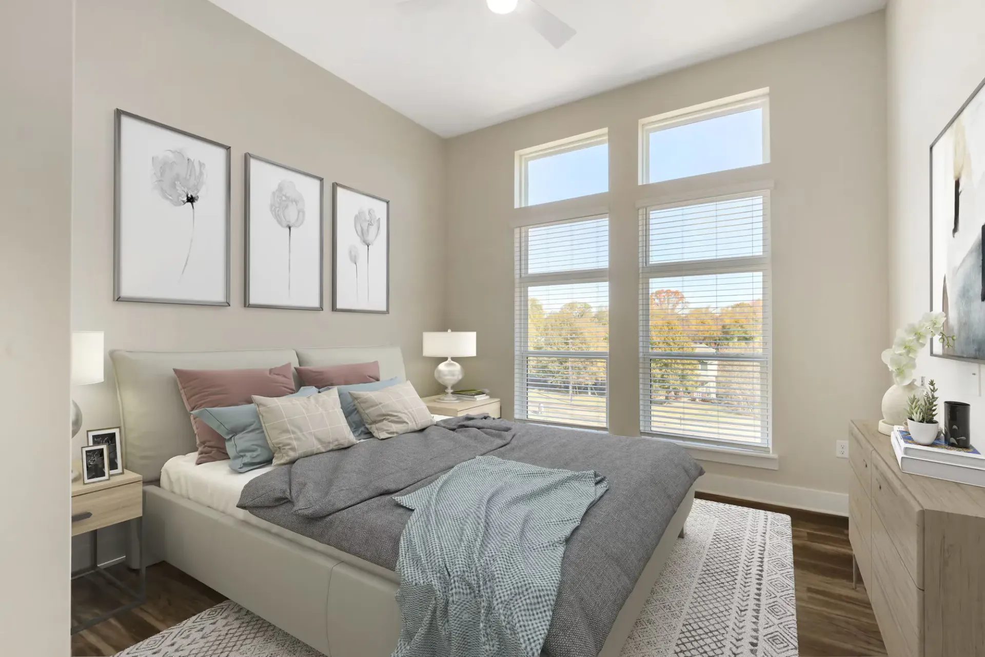 Bedroom inside an apartment with a large window, blinds, and a gray bed with multiple pillows.