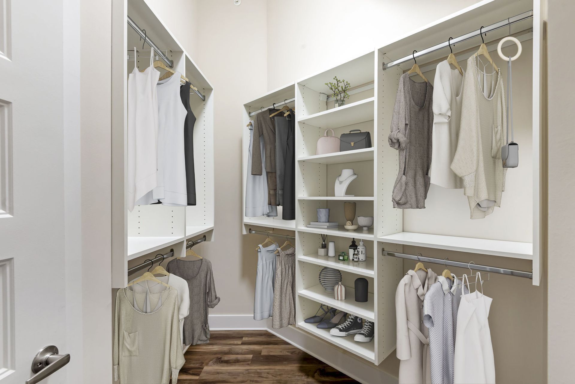 Walk-in closet with white shelving and rods holding various clothing items. Wooden floor, neutral walls.