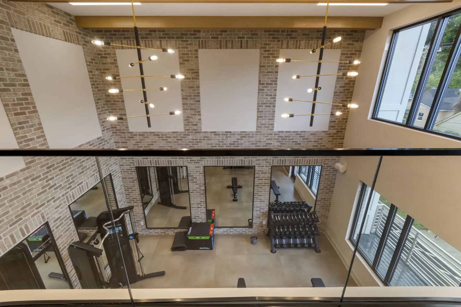 Brick-walled community gym with weight rack, machines, mirrors, and large windows.