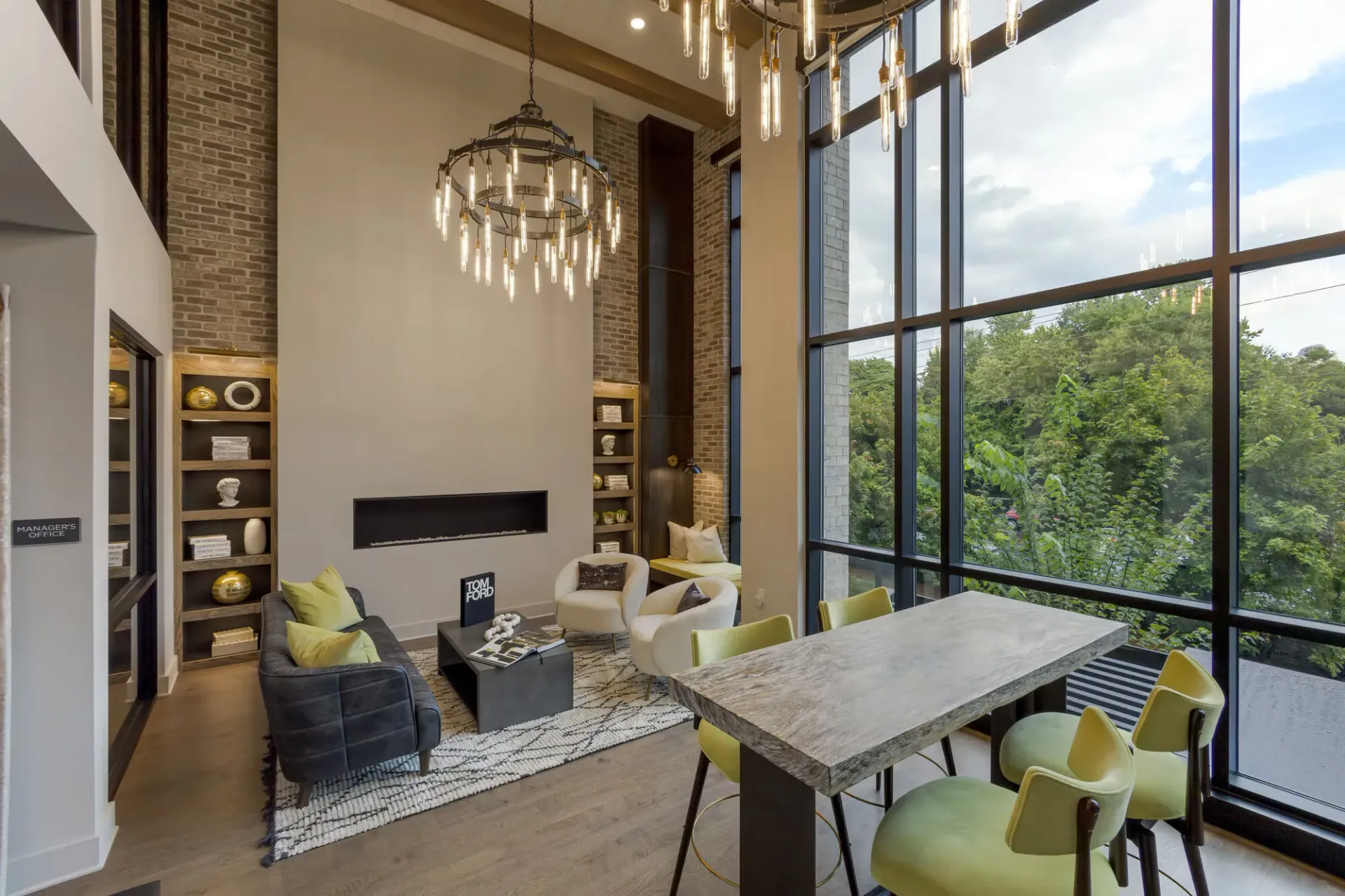 Modern apartment community lounge with tall glass windows, chandelier, and seating area.
