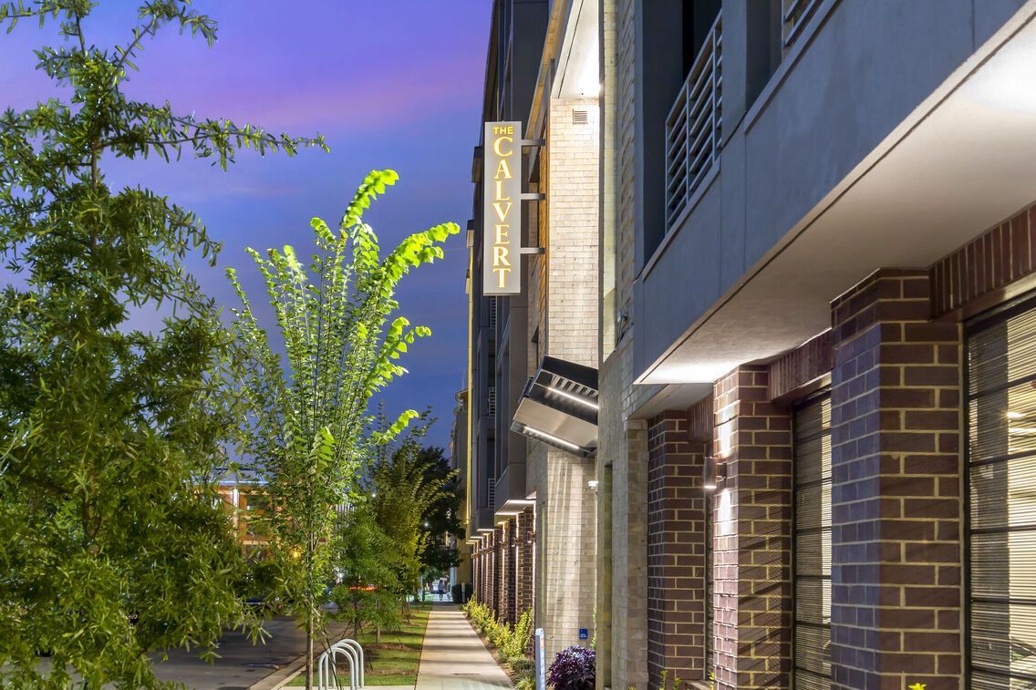 Exterior view of The Calvert apartment building at dusk with signage and landscaped sidewalk.