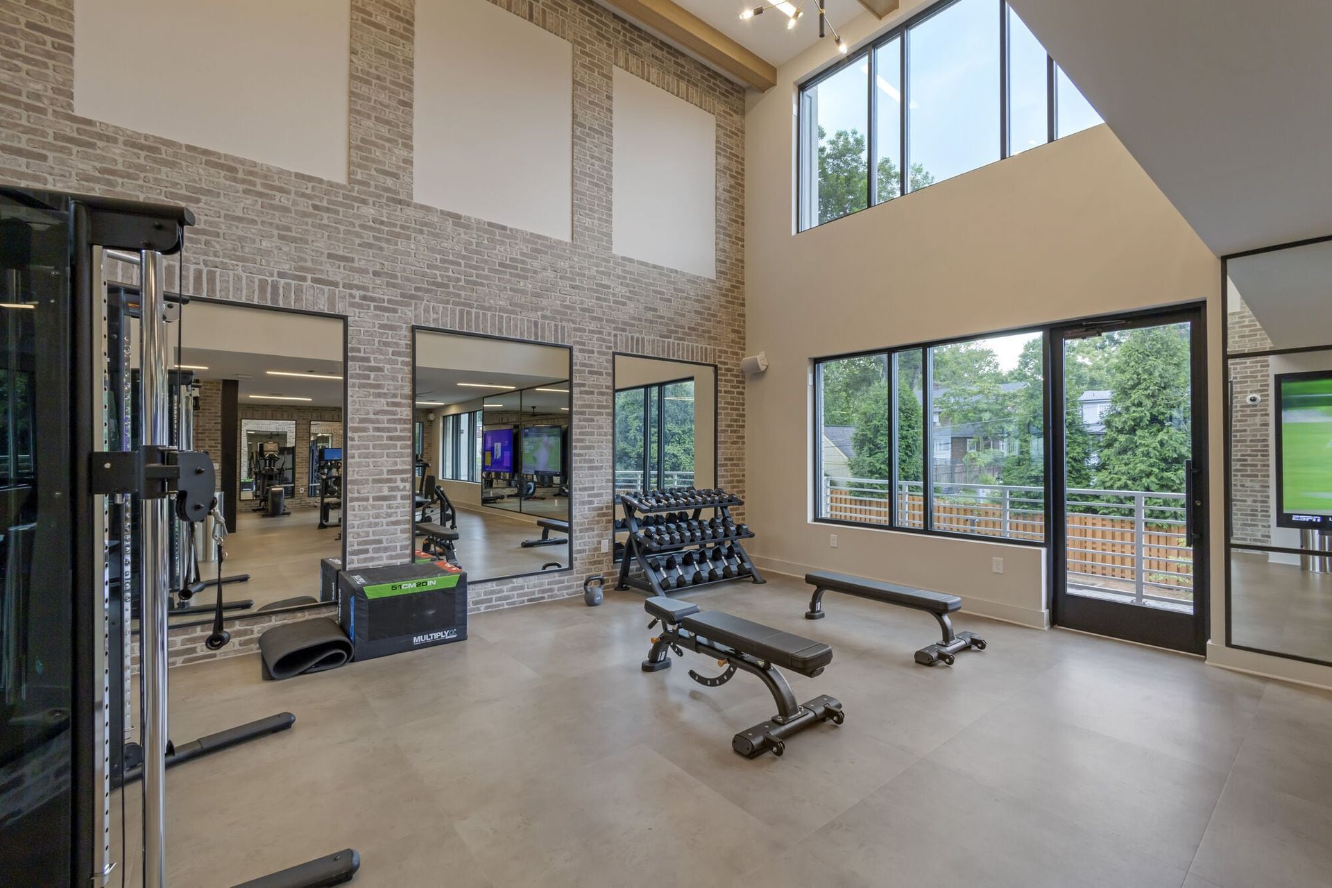 Bright modern fitness center with free weights, benches, mirrors, and large windows.