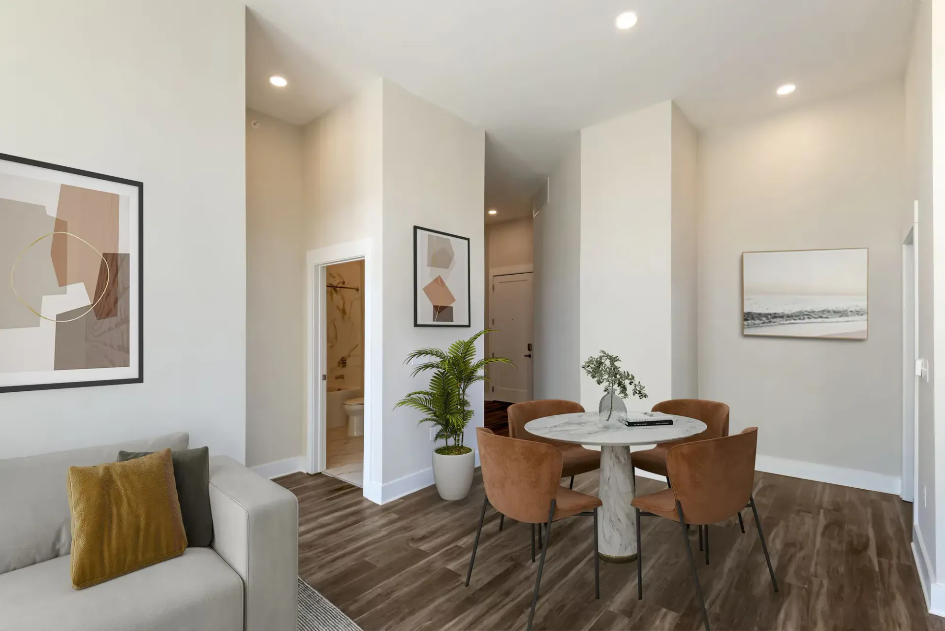 Interior living area with round marble dining table, brown chairs, sofa, plants, and abstract art.