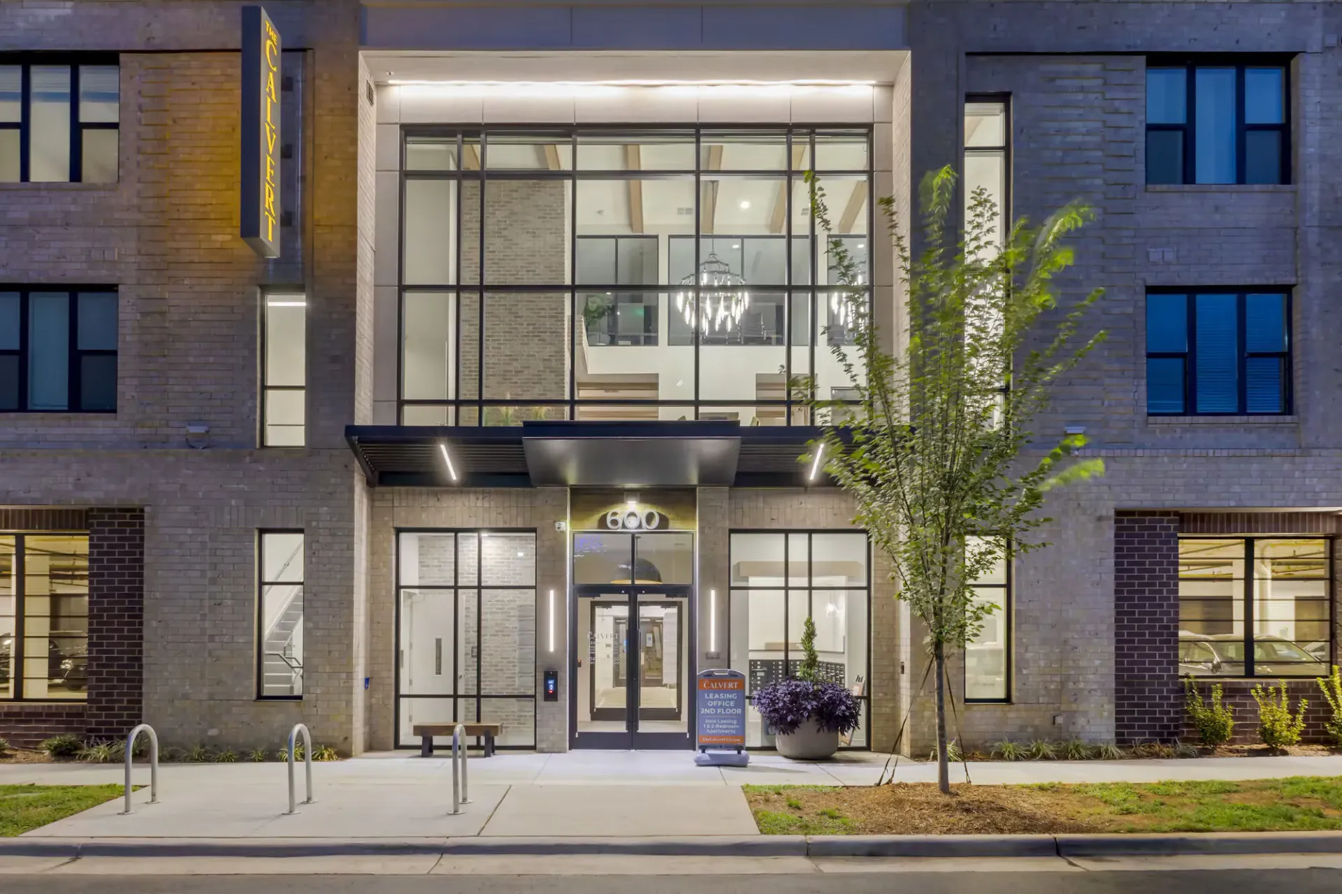 Exterior of apartment building entrance with a large glass storefront and landscaping.