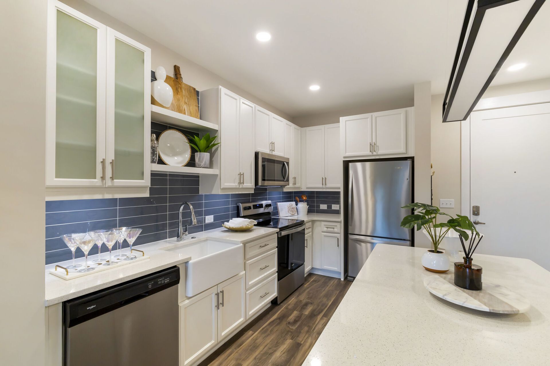 Bright modern kitchen with white cabinets, stainless appliances, blue tile backsplash, and an island.