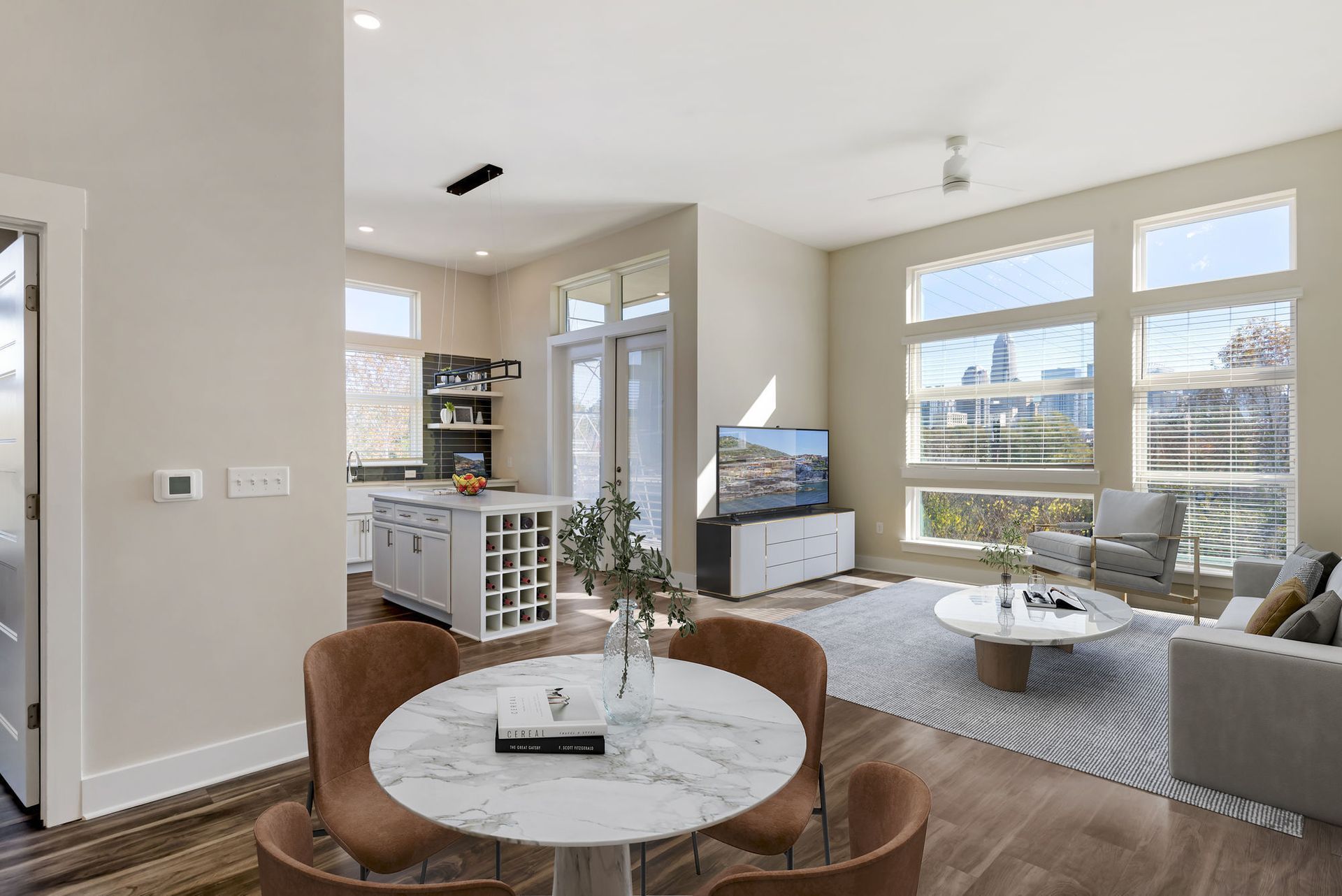 Open-concept living area with a marble dining table, kitchen island, and large windows.
