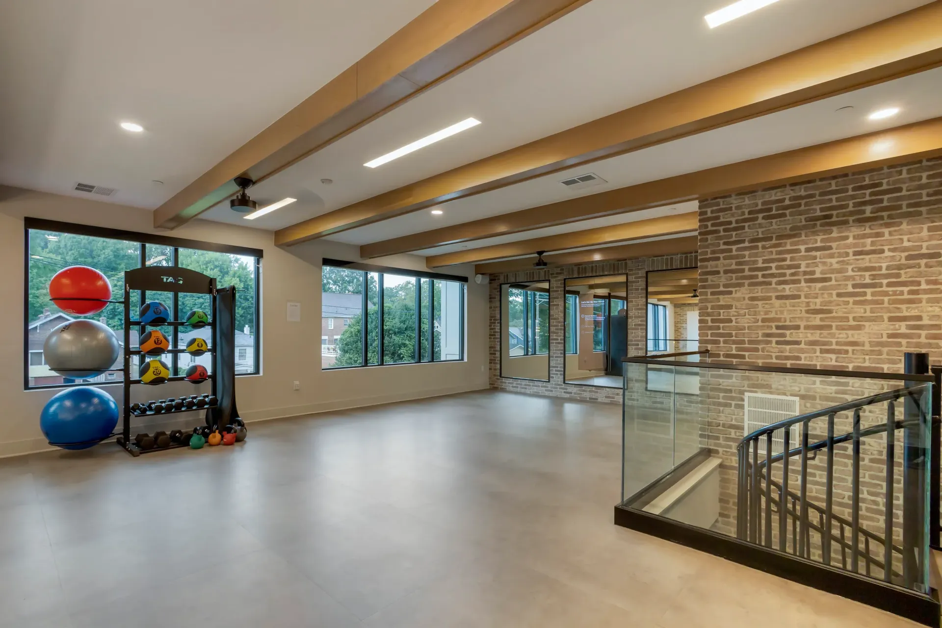 Spacious community gym with weight rack, medicine balls, and large windows.