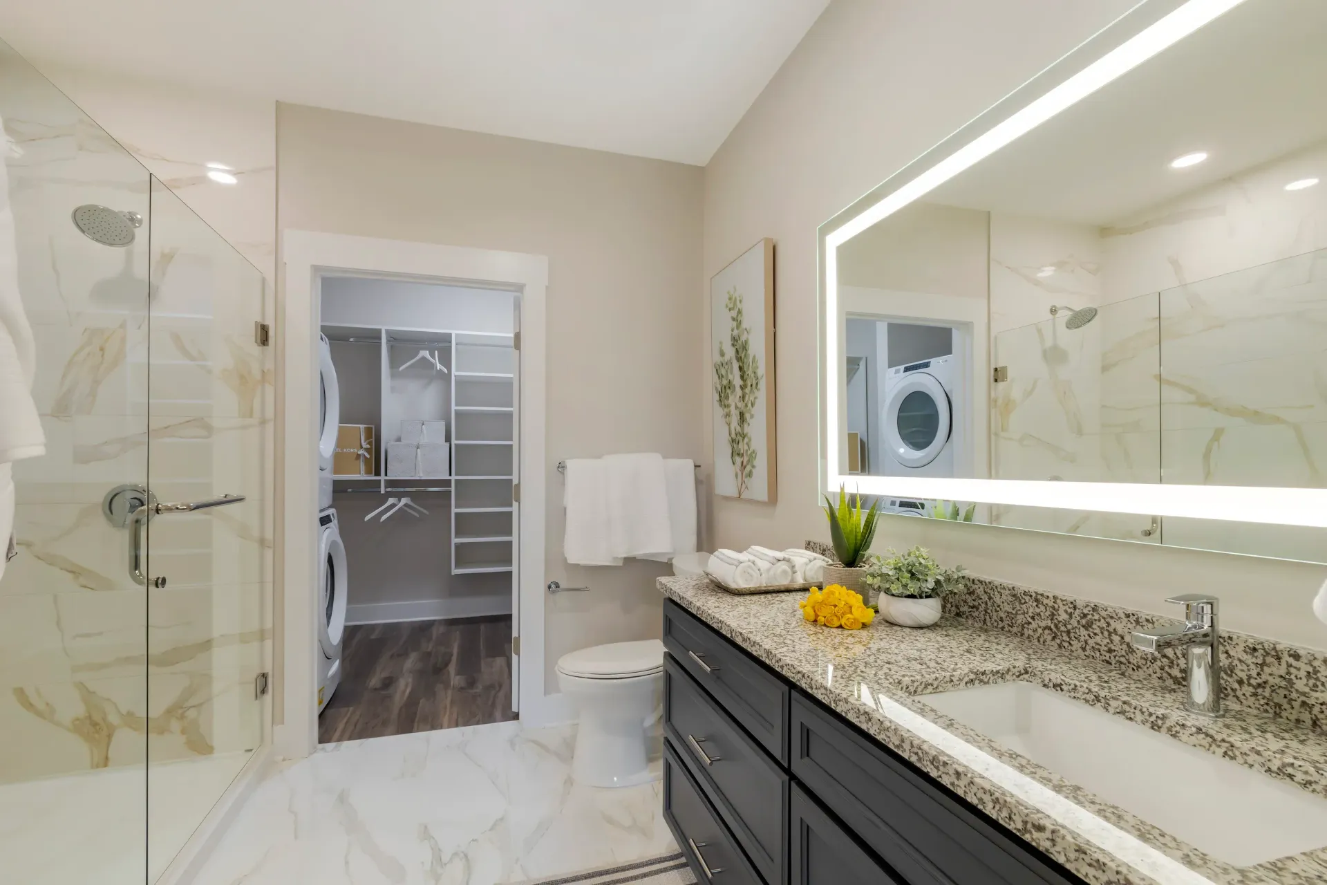 Modern bathroom with glass shower, granite vanity, and a stacked washer/dryer in a walk-in closet.