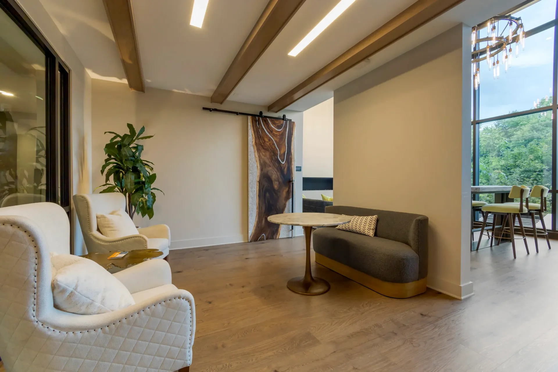 Interior resident lounge with beige armchairs, a gray sofa, a round marble table, and large windows.