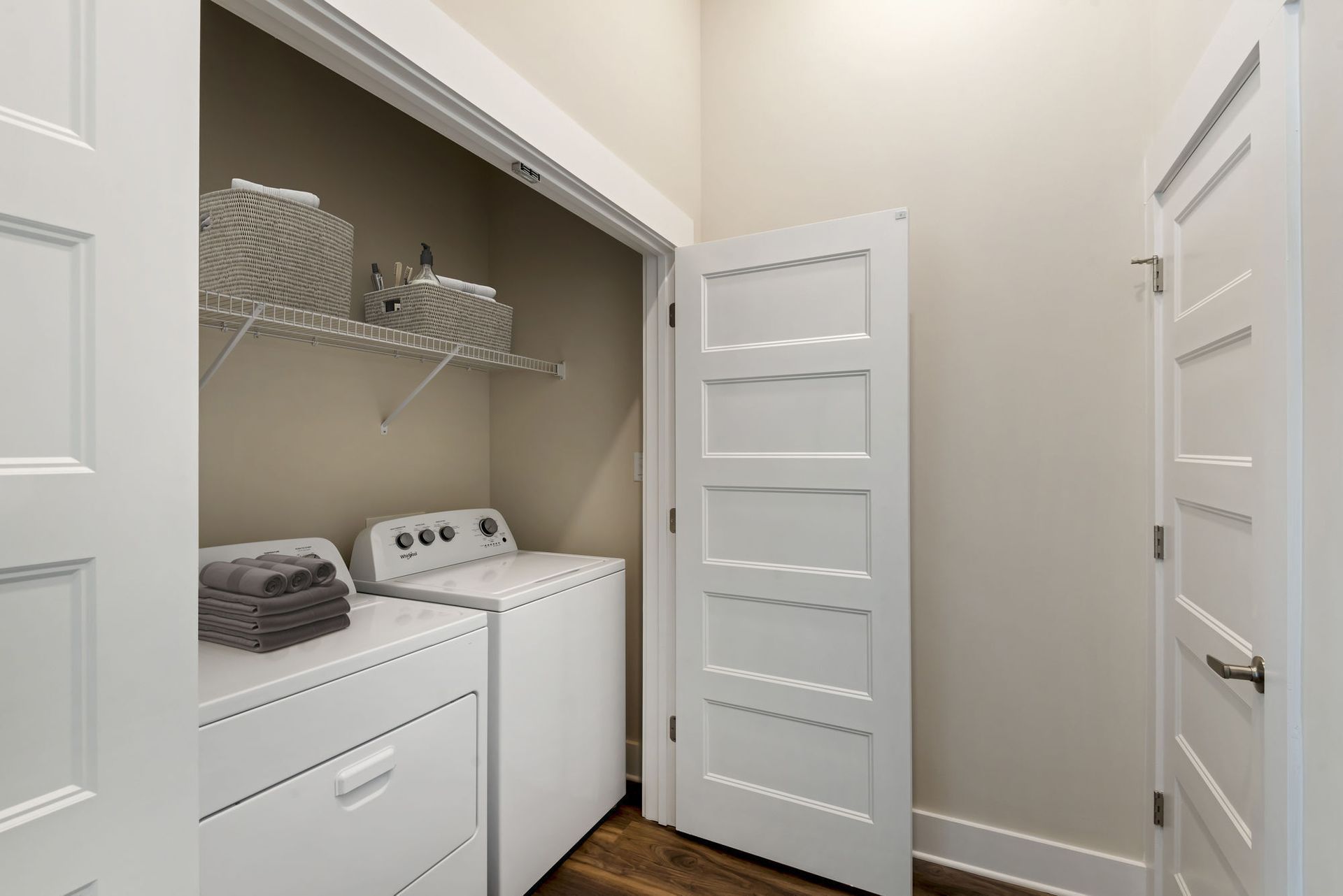 White washer and dryer in a small laundry closet with a wire shelf and baskets.