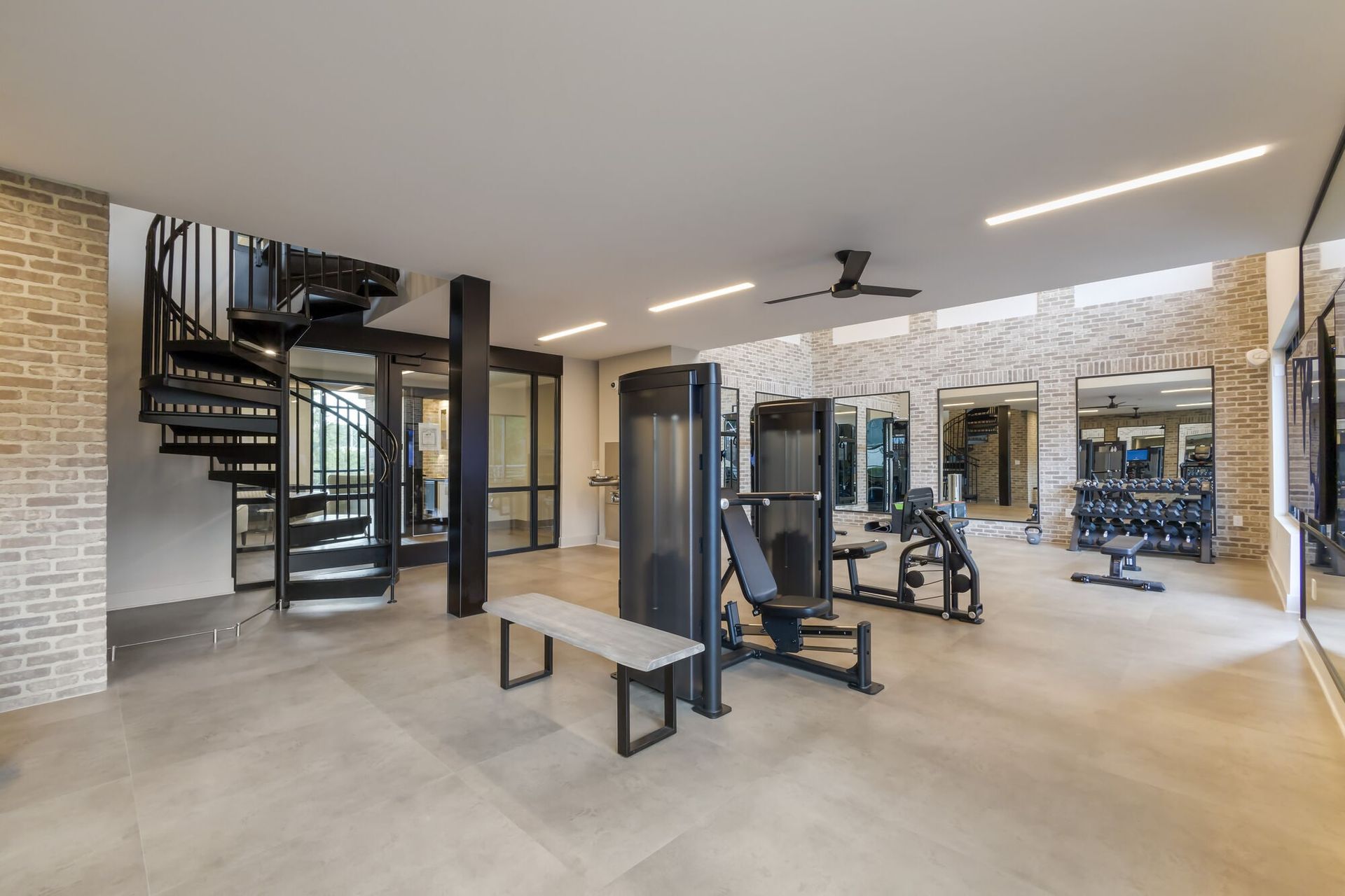 Interior of a community gym with weight machines, free weights, benches, and mirrors.