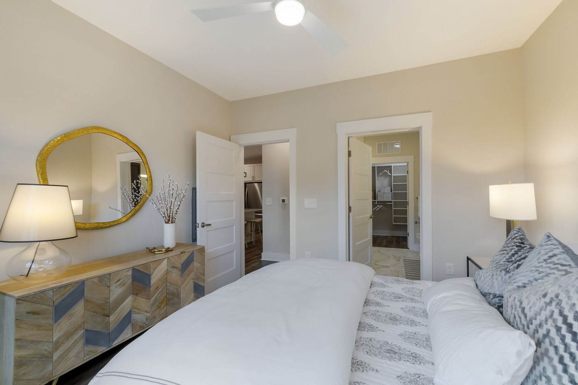 Bedroom in a modern apartment with bed, dresser, and two doors leading to a closet and hallway.