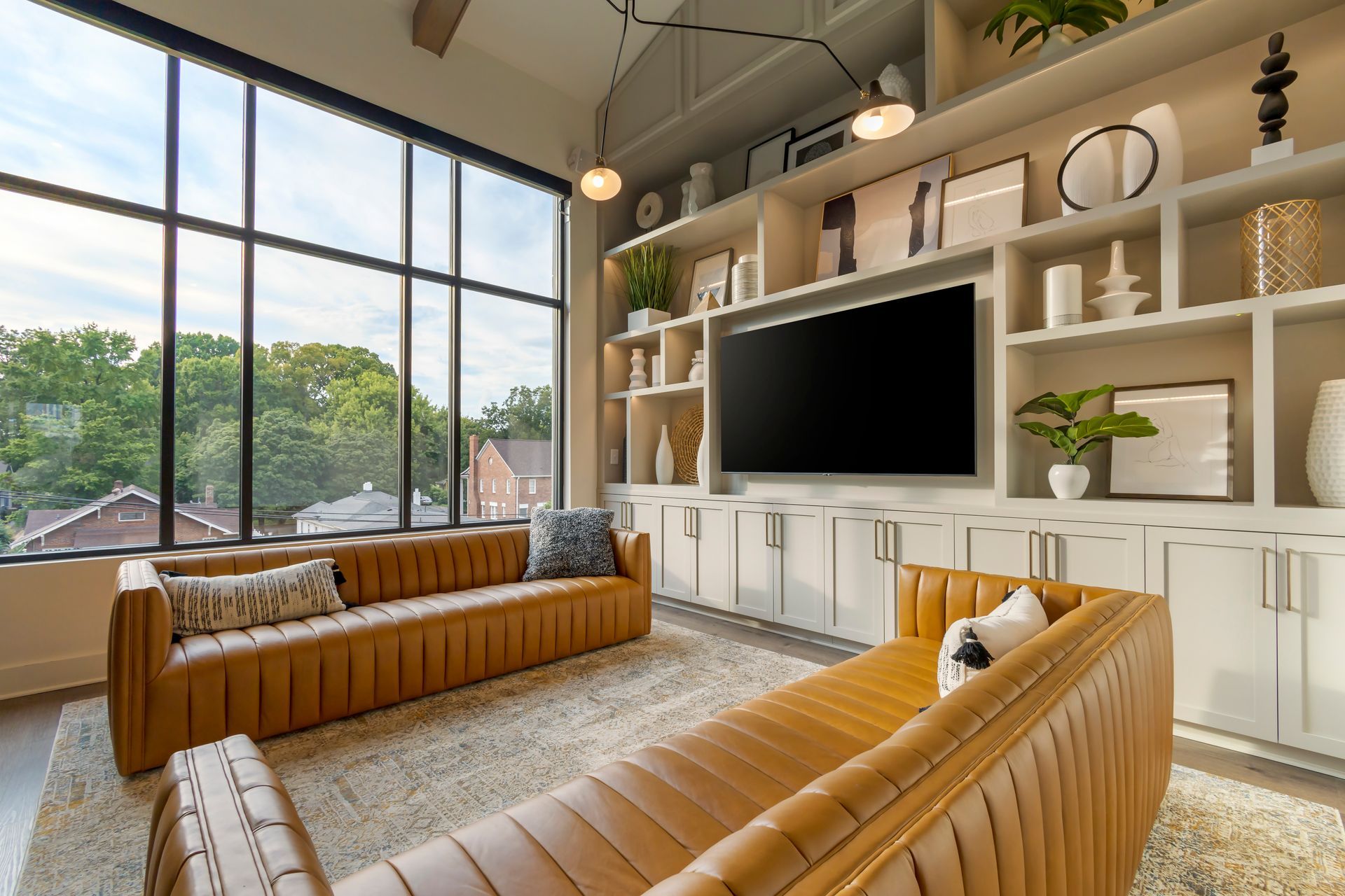 Living room with tan sofas, large window, built-in shelves, and TV.