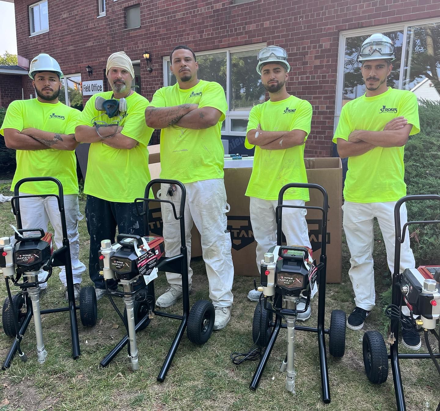 A group of men in neon yellow shirts are standing next to spray paint machines.