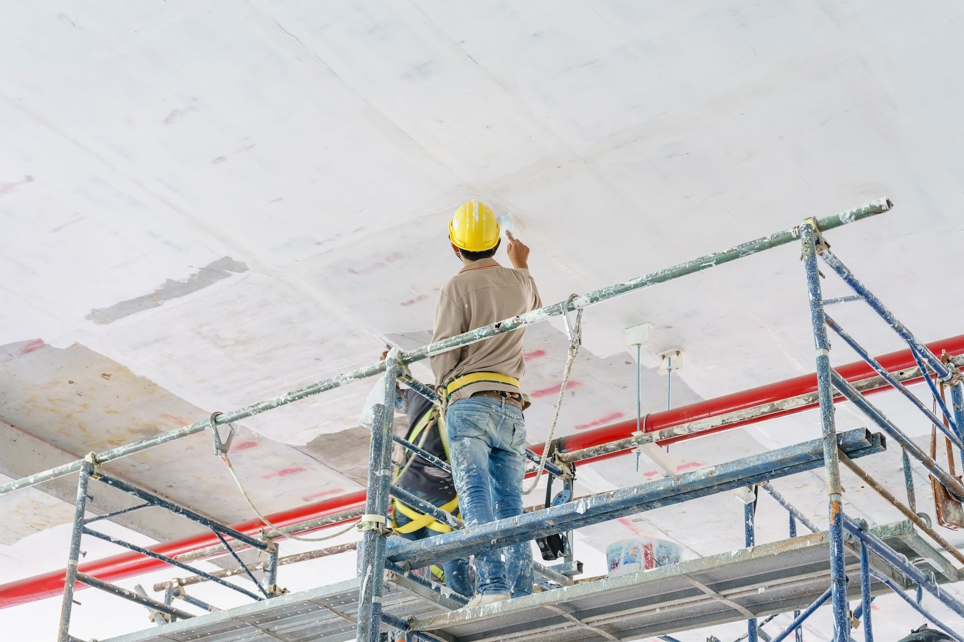 Painting company worker on scaffold painting ceiling in commercial building renovation.