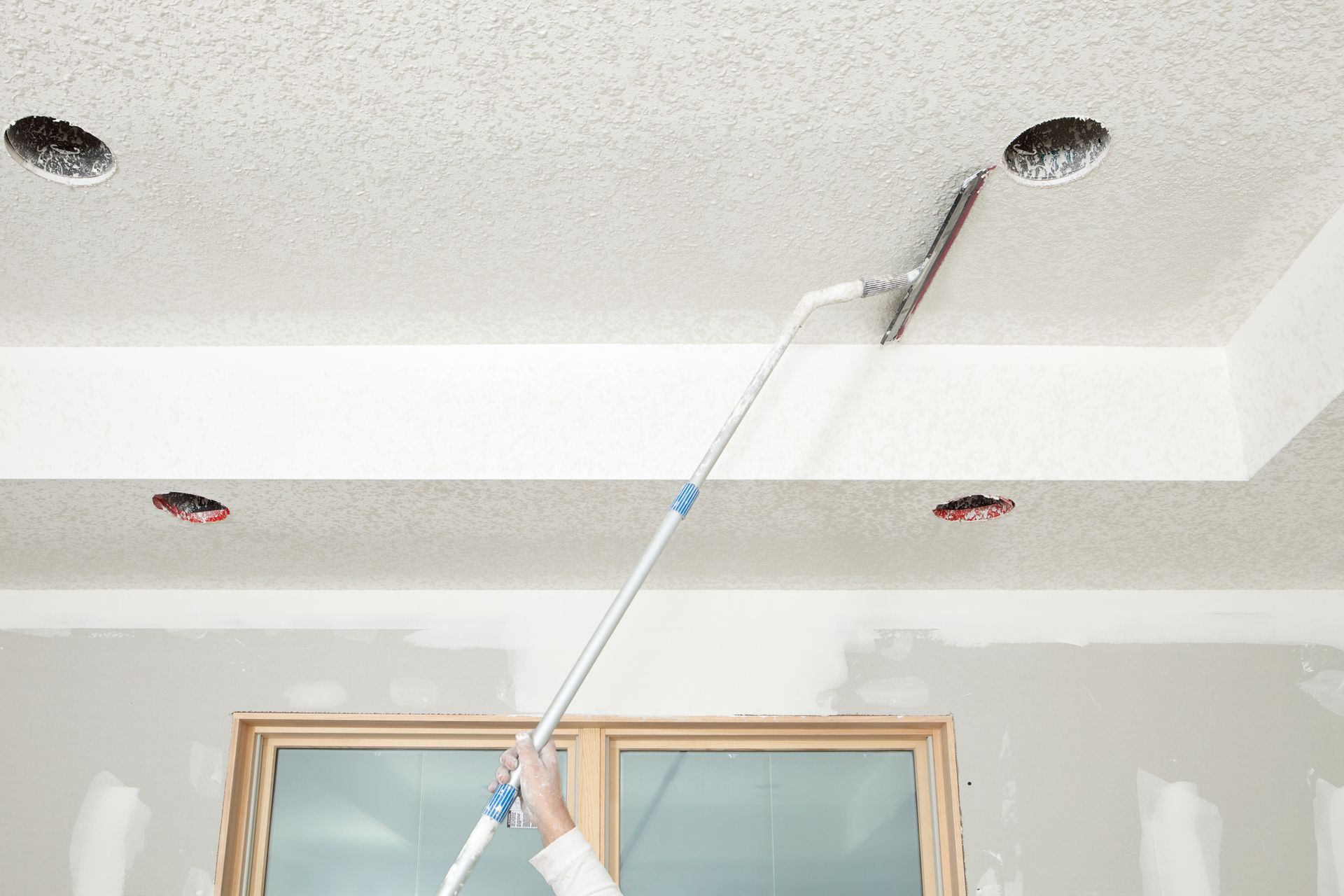 A person is removing wallpaper from a ceiling with a spatula.