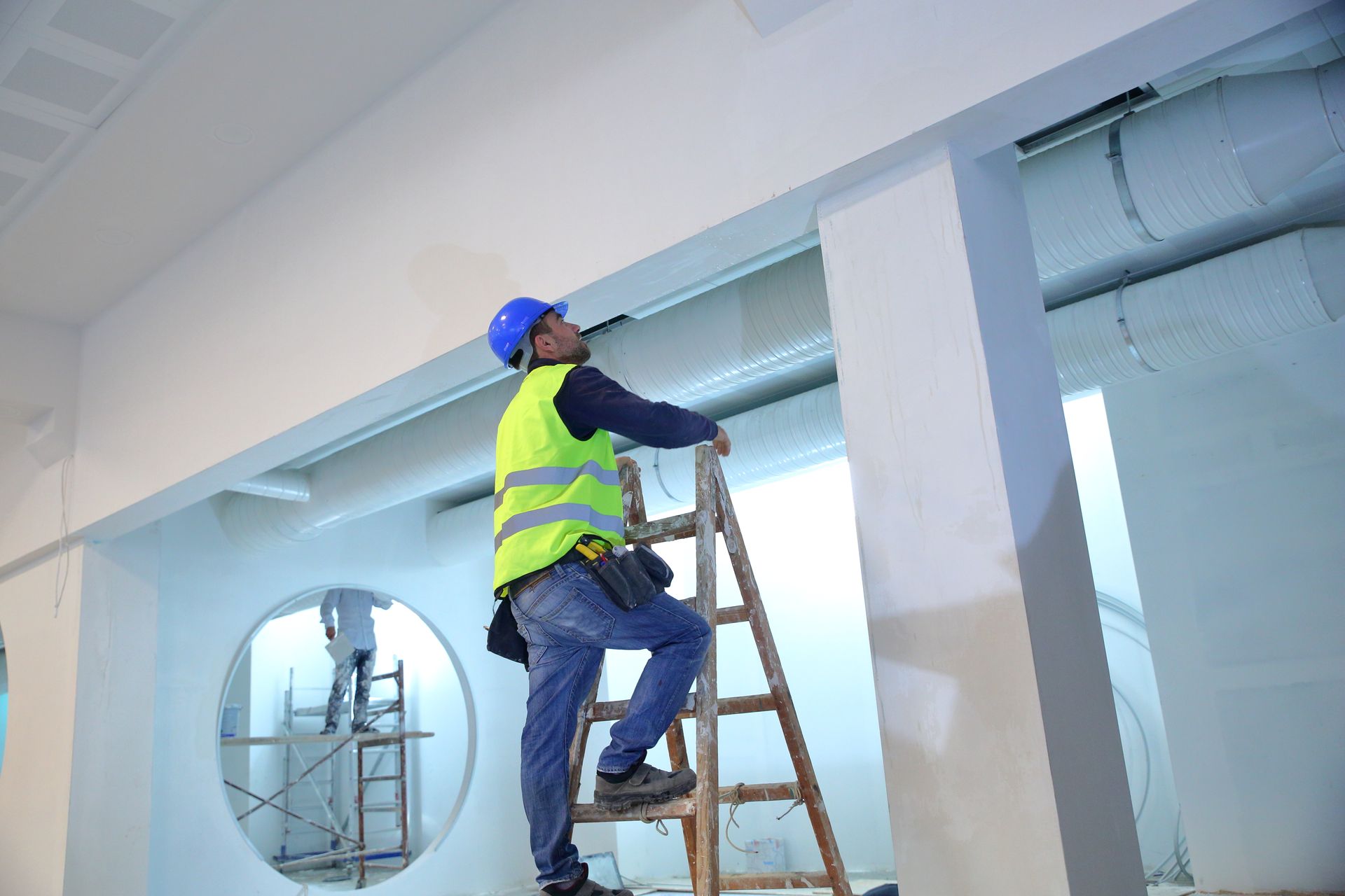 A man is standing on a wooden ladder in a room.