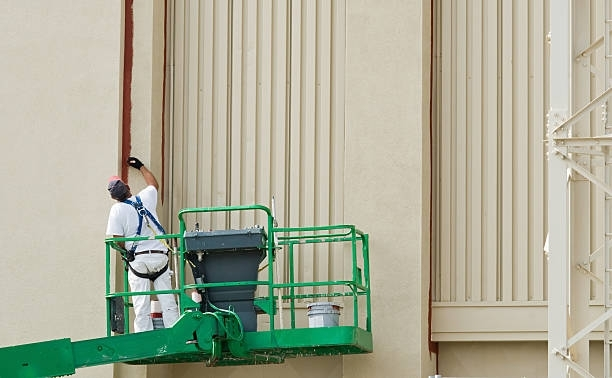 A man is painting a building from a crane.