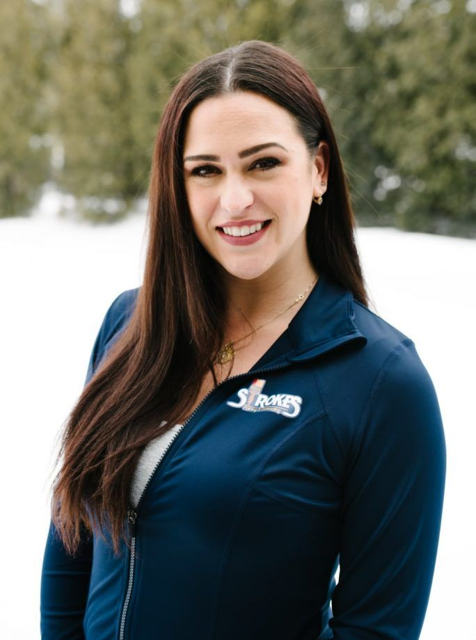 Woman with long dark hair smiles in front of snowy background, wearing a navy jacket with white logo.