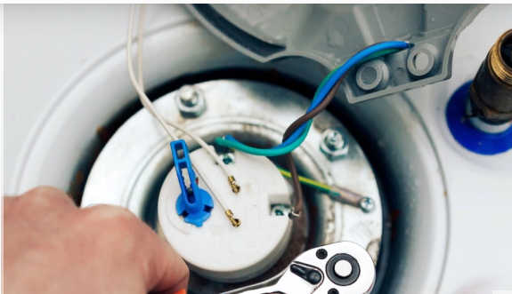 Hand using wrench to work on electrical components inside a water heater, with wires visible.