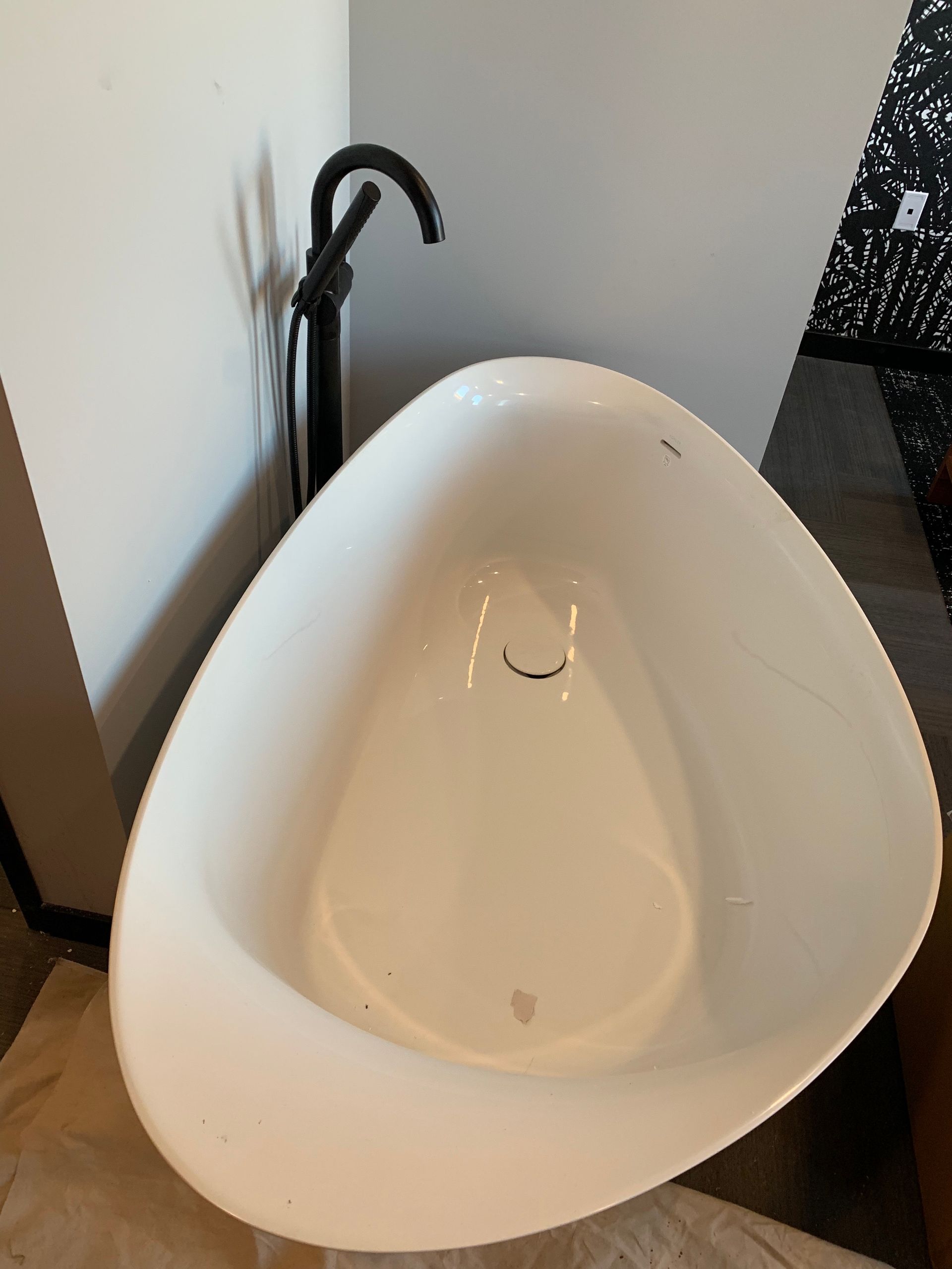 White, teardrop-shaped bathroom sink with black faucet against a white wall.