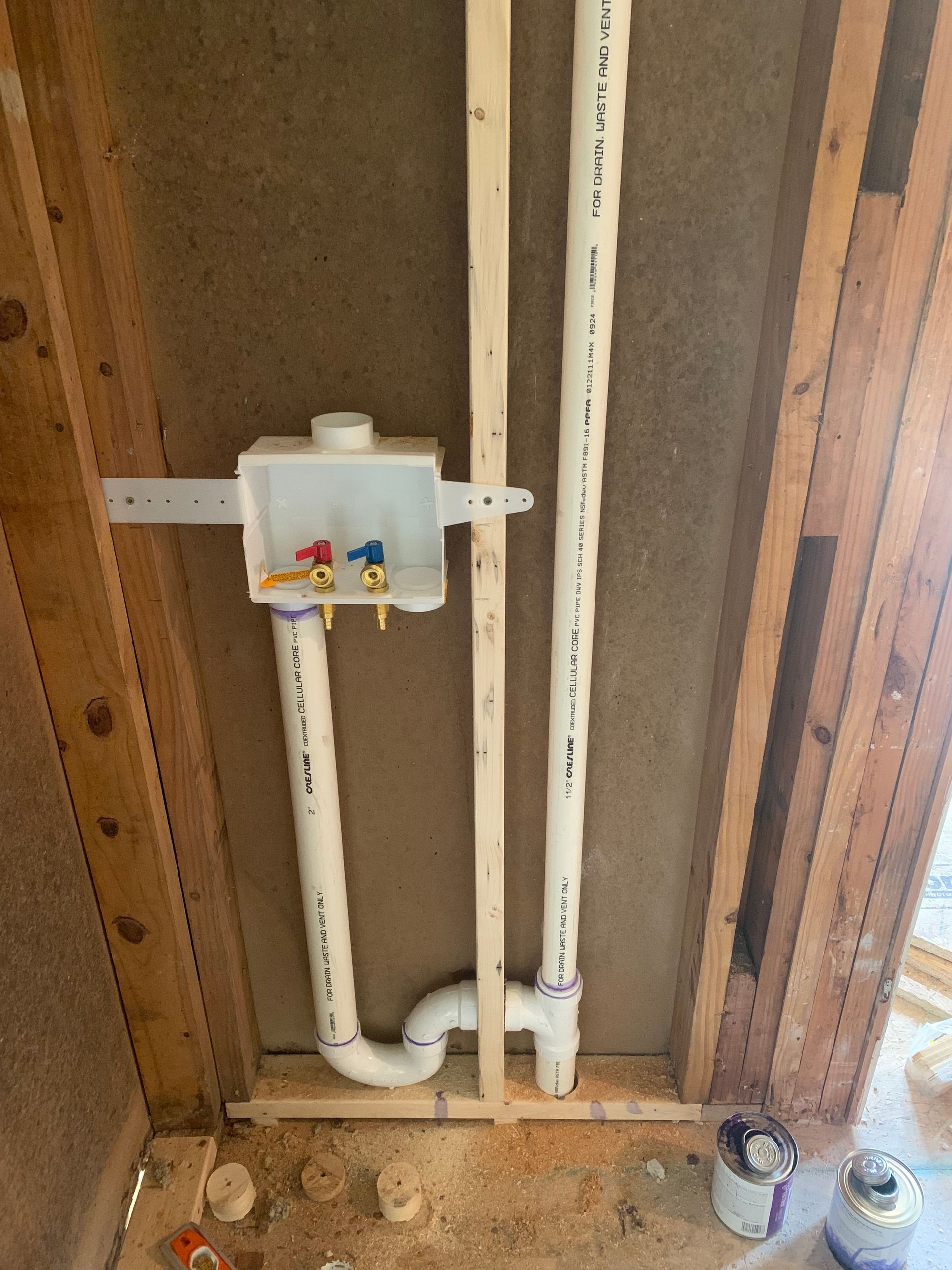 Laundry room plumbing with hot and cold water pipes, drain pipe, and wall box within wood framing.