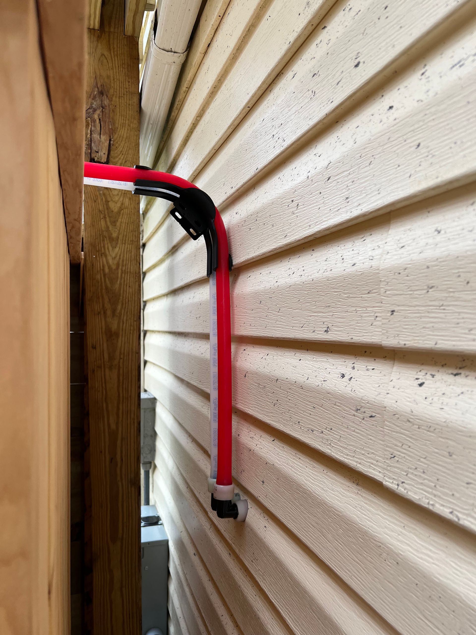 Red electrical conduit bends around corner of siding.