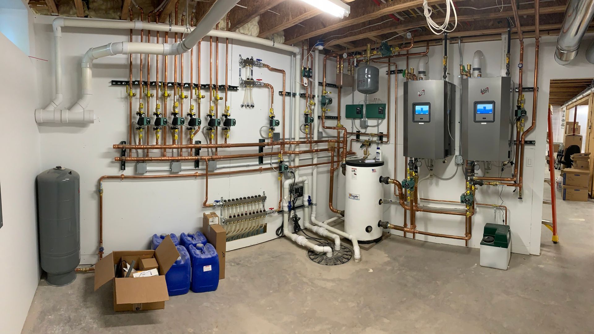A utility room with complex copper piping, two water heaters, and various plumbing components.