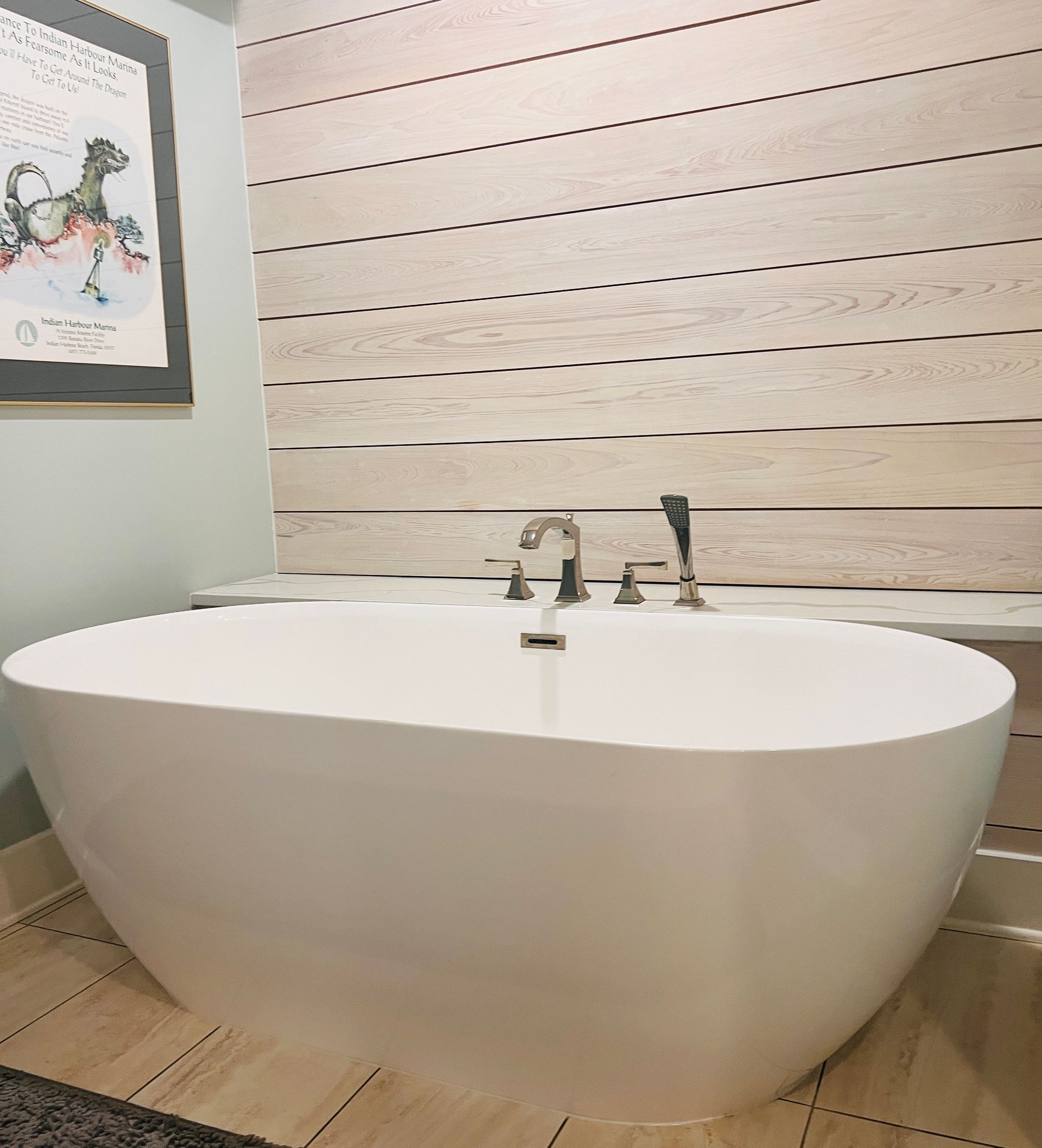 White oval bathtub in a modern bathroom, set against wood-paneled wall, near a framed art piece.