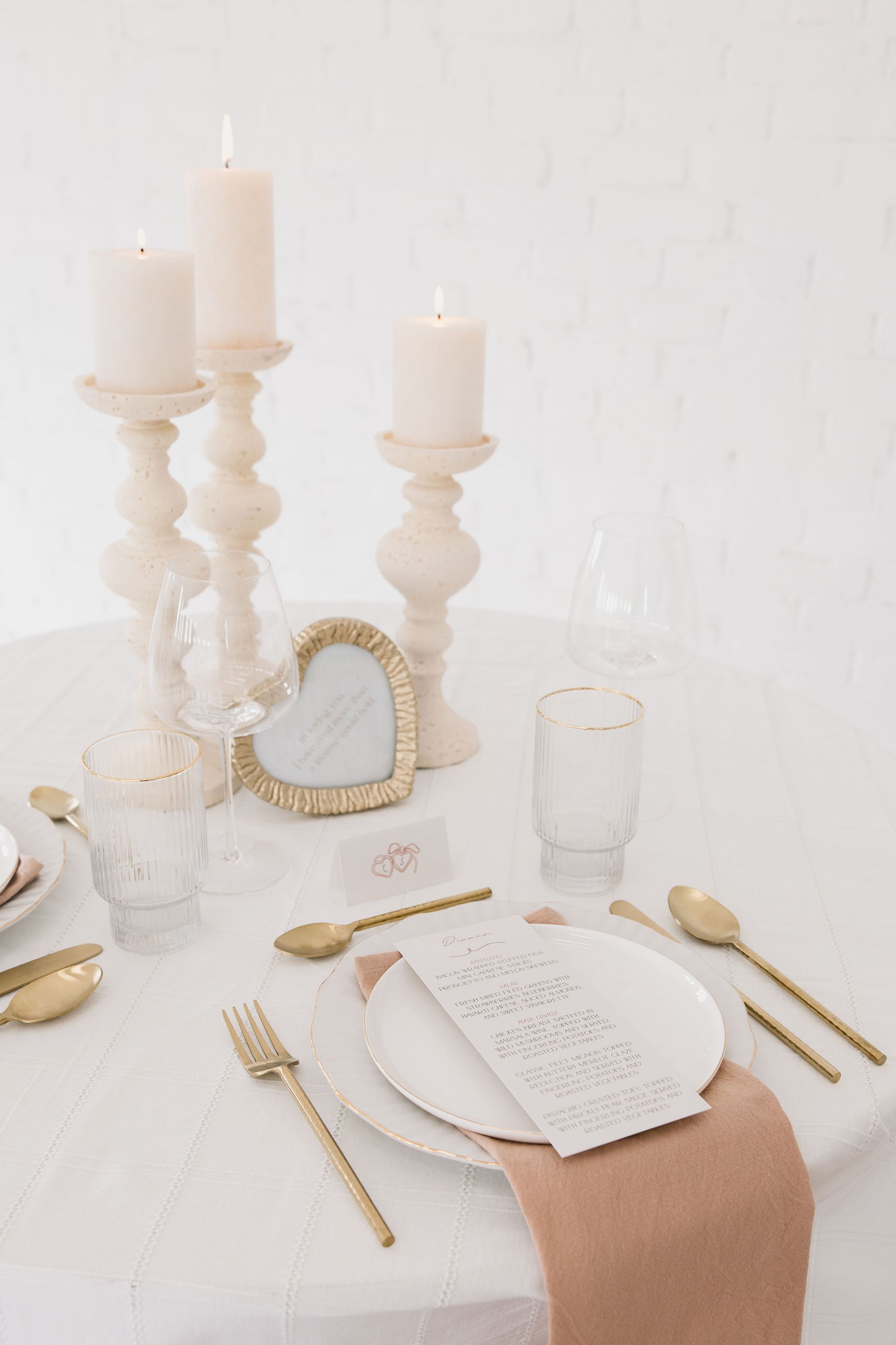 A table set for a wedding reception with plates , silverware , candles and glasses.