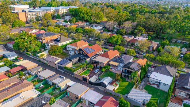 Aerial view of a suburban neighborhood with red-roofed houses, tree-lined streets, and dense greenery.