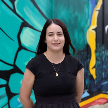 Woman standing before a colorful mural with teal, black, and yellow geometric shapes.