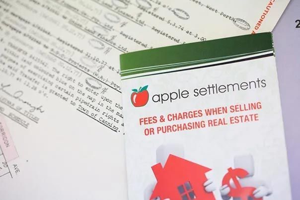 Apple Settlements brochure on fees and charges for purchasing real estate, with papers in the background