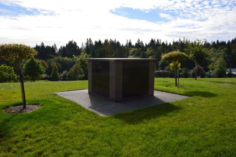 Dark stone memorial in a grassy park with trees and a cloudy sky