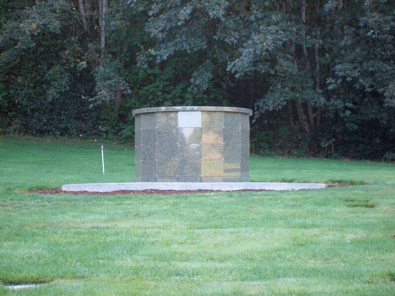 Small stone memorial structure on a grassy lawn with trees in the background