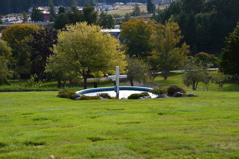 White cross monument in a green park with trees and a cityscape in the background