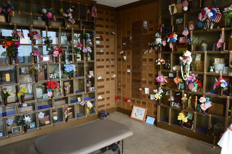 Wood-paneled room with shelves of small memorial items and flowers, like a shrine or display wall