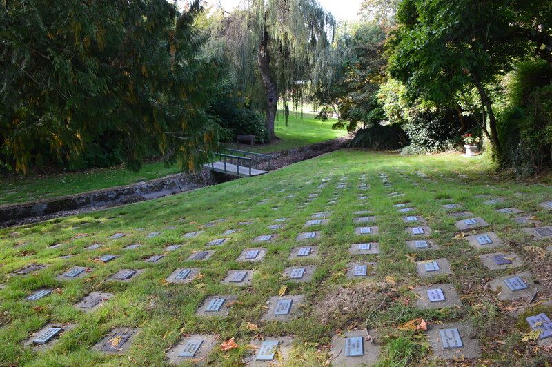 Grassy memorial lawn with rows of small plaque markers beside trees and a winding path